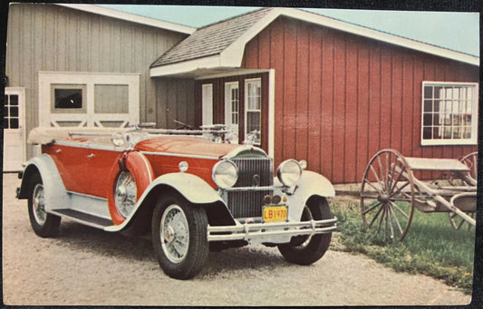 Vintage car parked in front of a red barn with a wagon nearby.