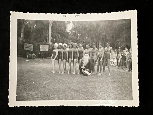Vintage black and white photo of a line of people in bathing suits standing on a grassy field.