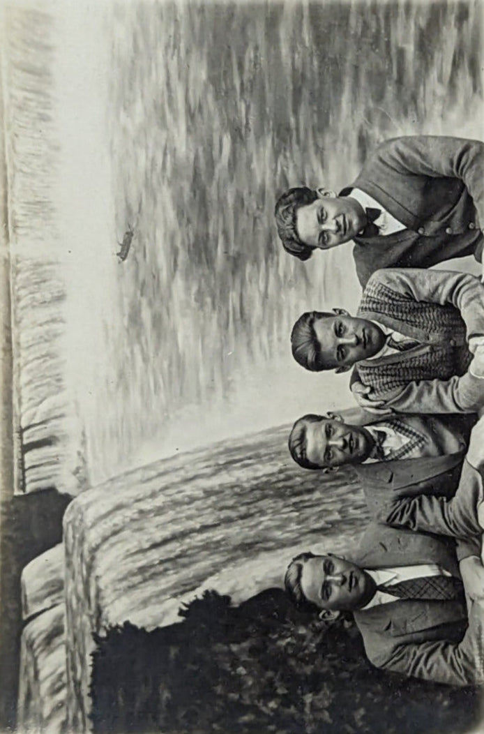 A black and white photo of a group of four young men posing at Niagara Falls. They are dressed in suits and ties