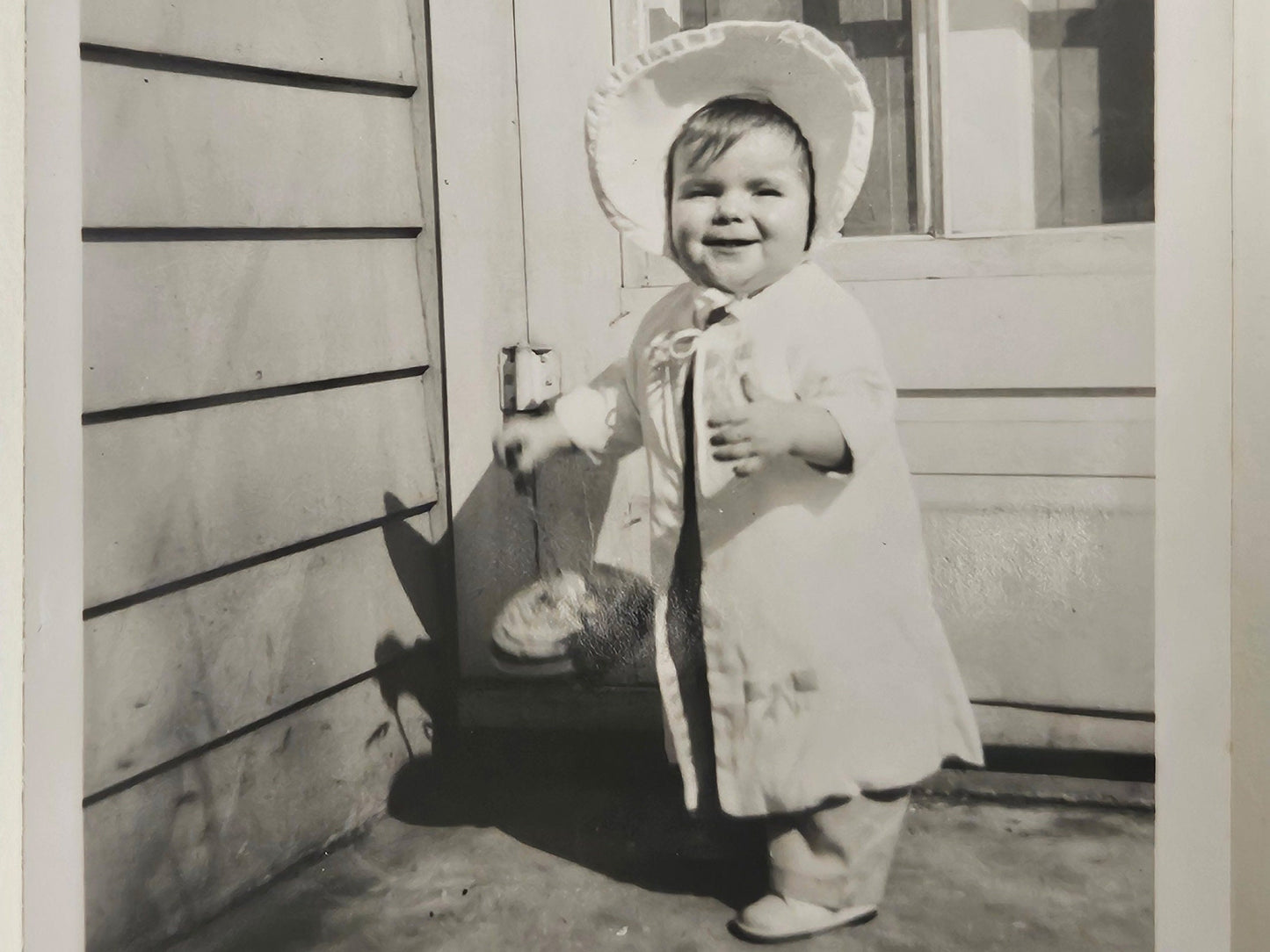 Baby Girl In White Outfit with Sun Bonnet- Holding a large Top Smiling - Spring Baby Photo - Black and White Photograph 1950s