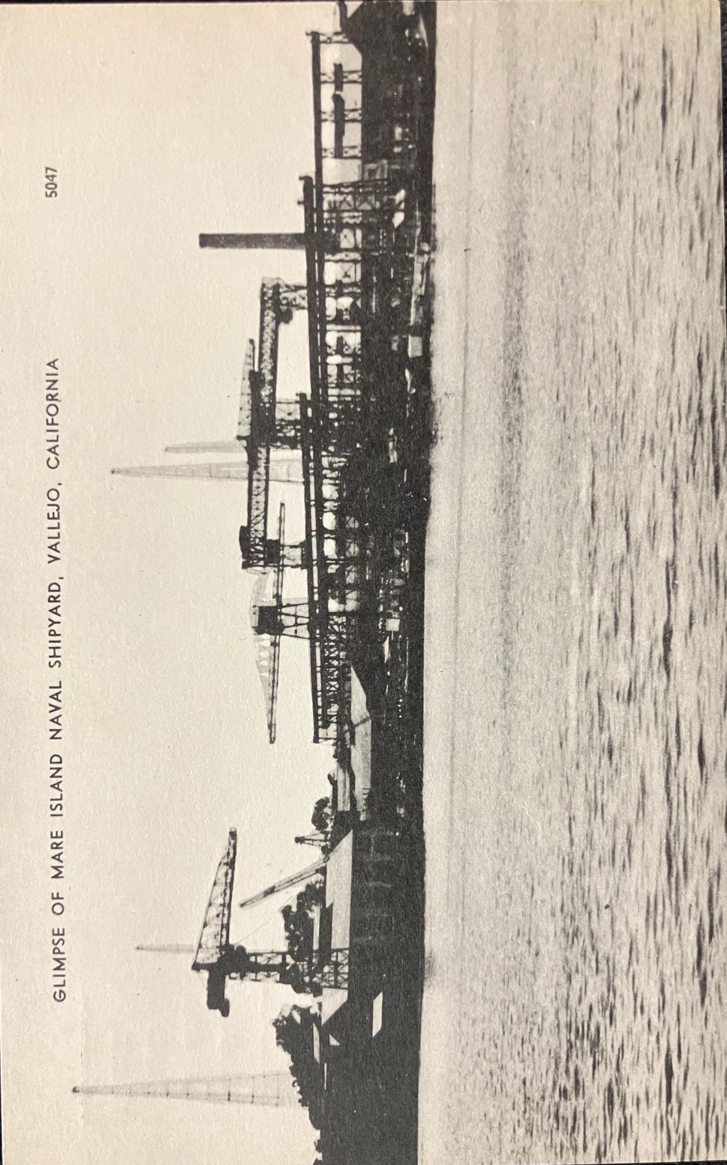 Black and white image of a shipyard with ships and structures on a beach.
