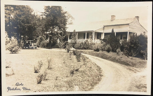 Vintage black and white photo of a house with a driveway and trees in the background