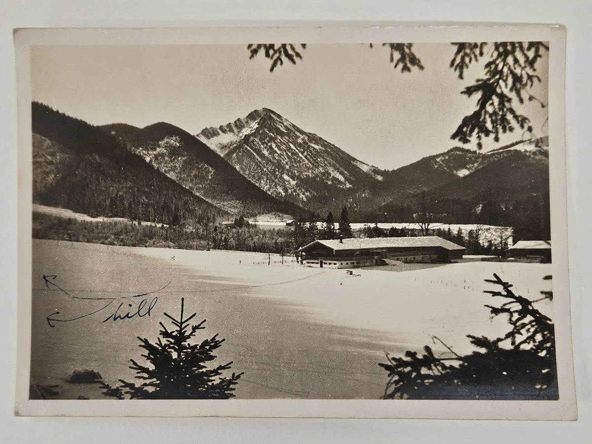 Vintage black and white photograph of a snowy landscape with mountains and a building.