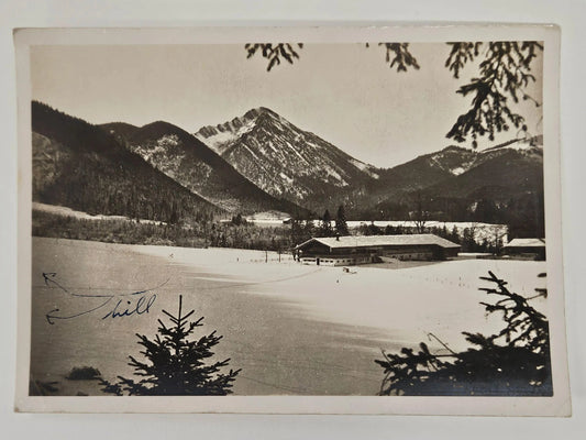 Vintage black and white photograph of a snowy landscape with mountains and a building.