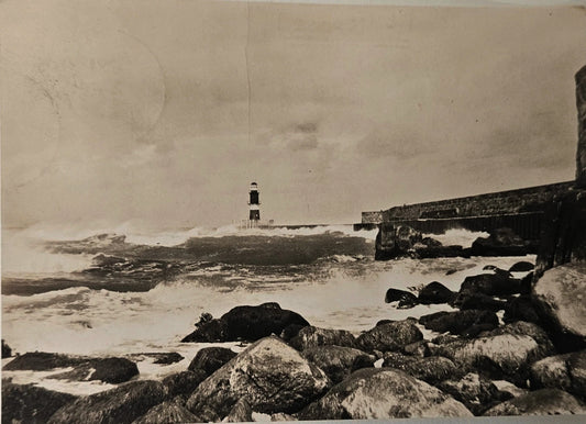 Black and white photograph of a rocky shoreline with a small boat in the distance.
