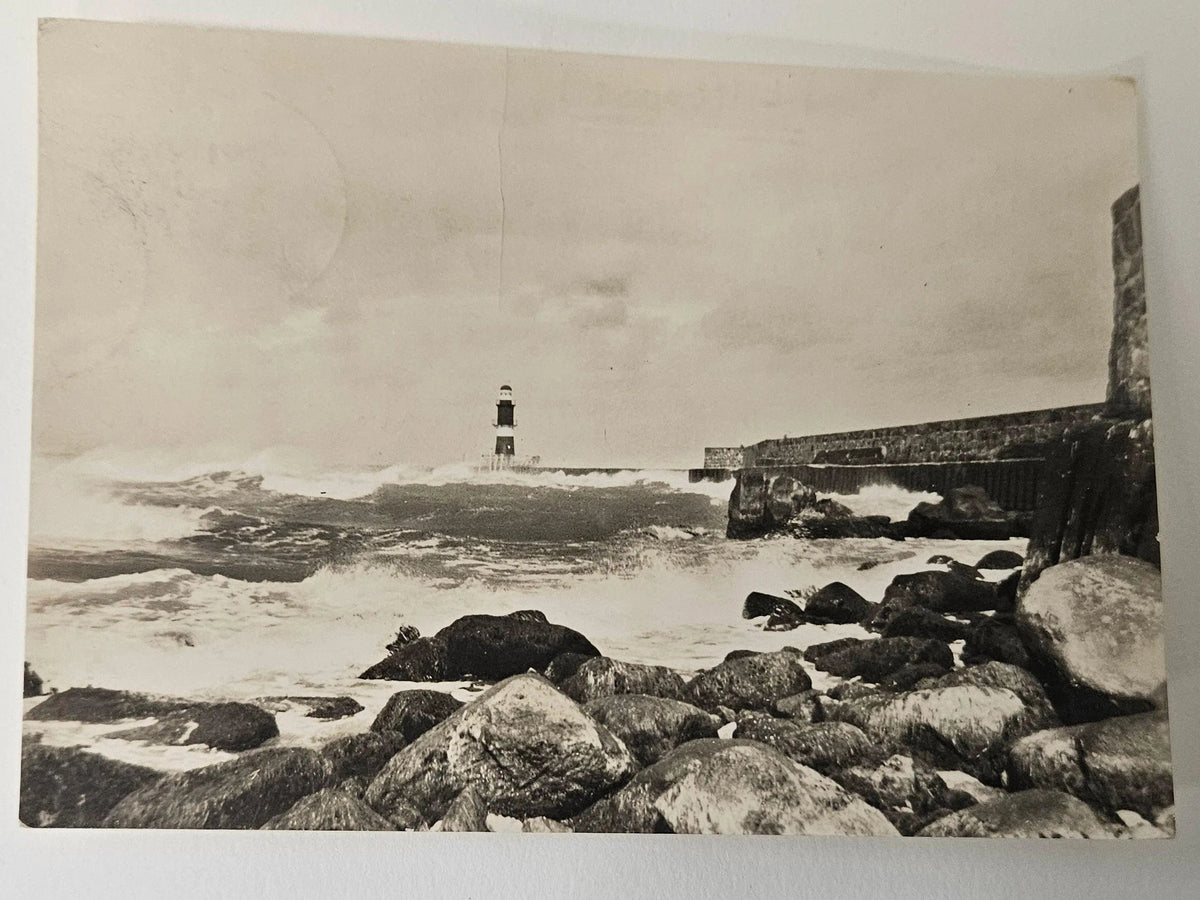 Vintage black and white photograph of a lighthouse surrounded by waves and rocks.
