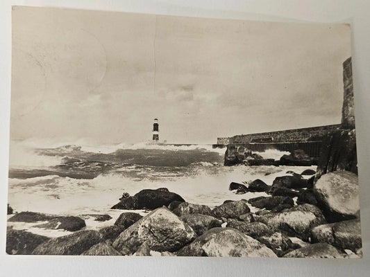 Vintage black and white photograph of a lighthouse surrounded by waves and rocks.