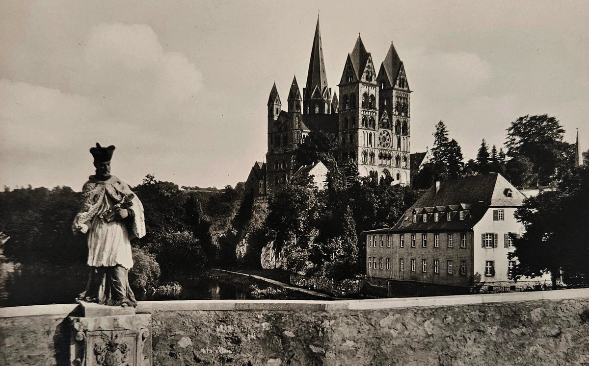 Black and white photo of a statue in front of a castle-like building with trees.