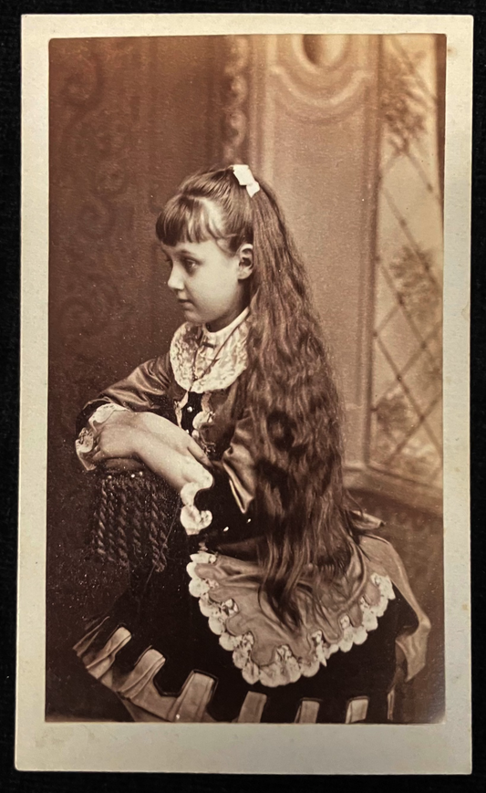 Vintage sepia-toned photograph of a young girl with long hair sitting on a chair.