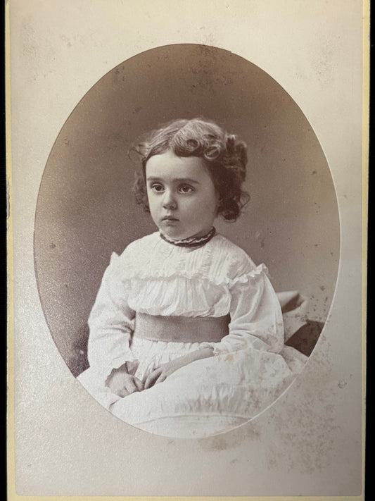 Vintage black and white portrait of a young girl in a white dress with ruffled collar.