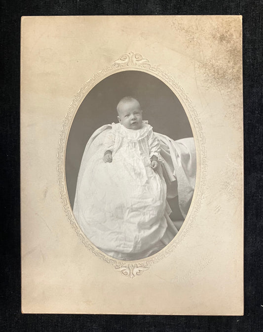 Vintage photograph of a baby in a formal outfit with an ornate frame.