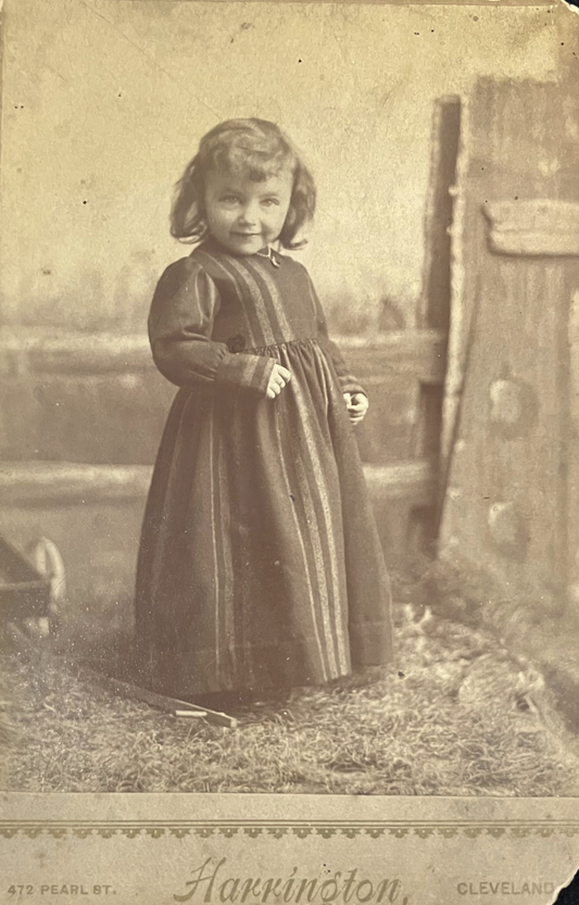 Vintage sepia-toned photograph of a young girl in a dress standing outdoors.