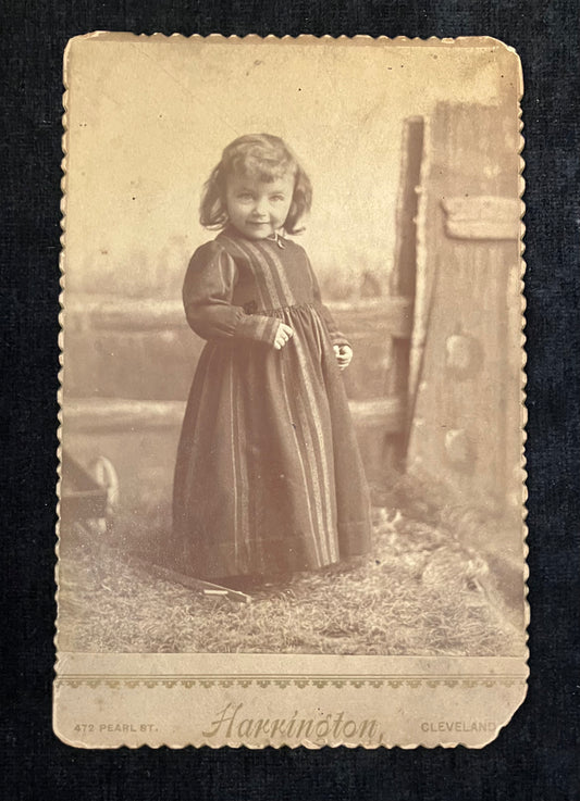 Vintage sepia-toned photograph of a young girl in a dress standing outdoors.
