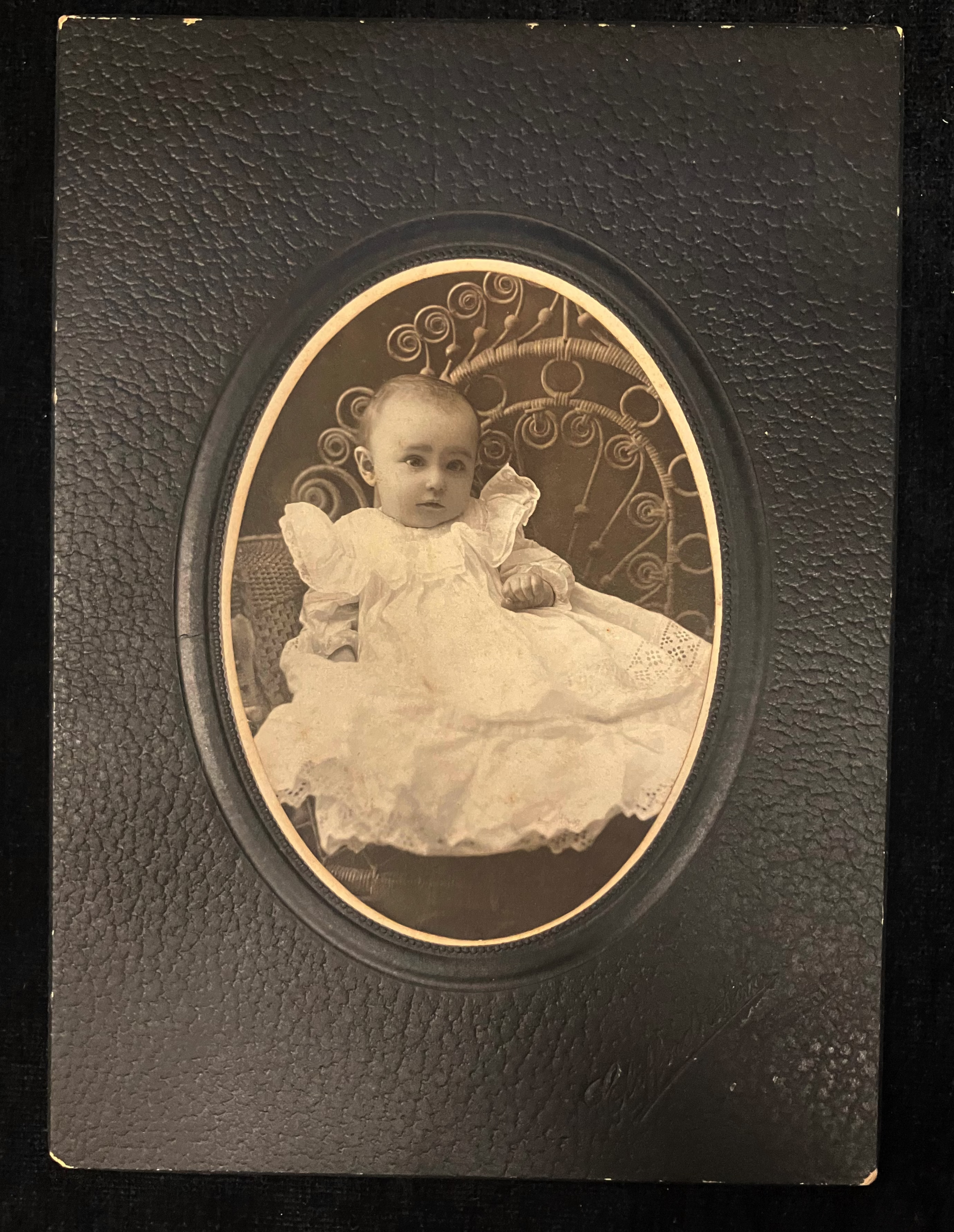 Vintage photograph of a baby in a decorative frame on a dark background