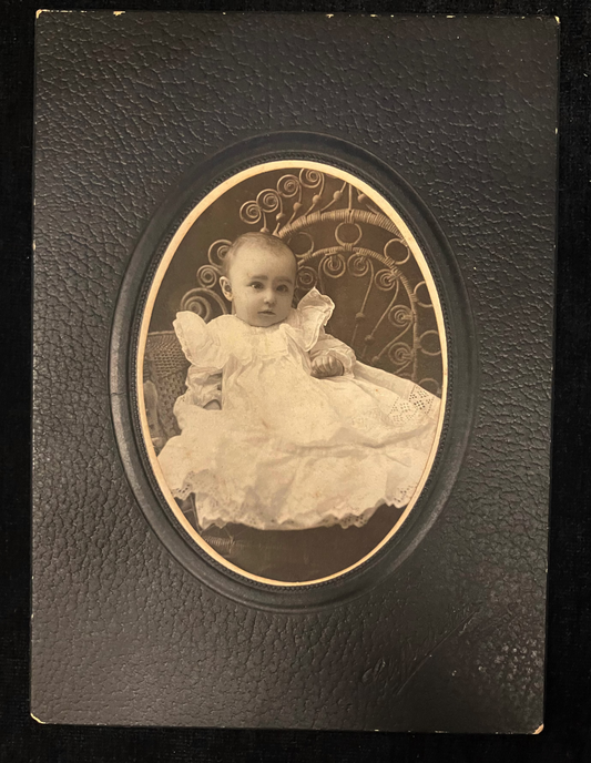 Vintage photograph of a baby in a decorative frame on a dark background