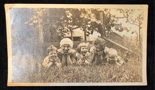 Vintage black and white photo of children sitting on grass with a tree in the background