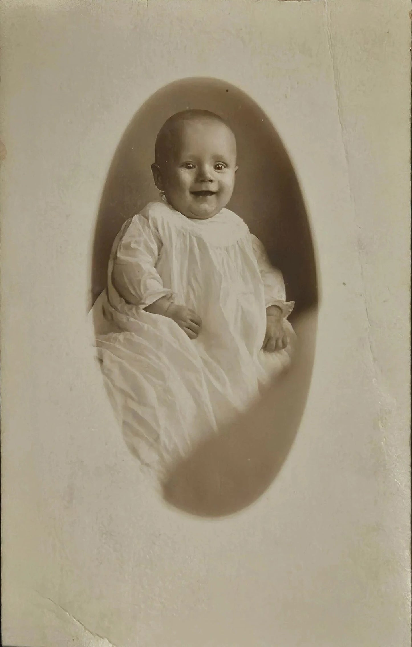 Vintage photograph of a baby in a white outfit against a plain background