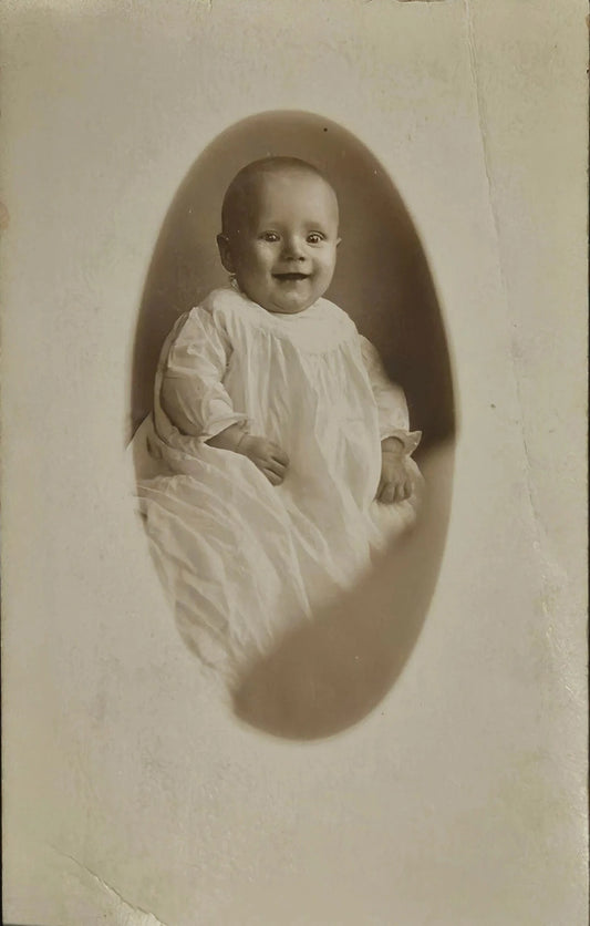 Vintage photograph of a baby in a white outfit against a plain background