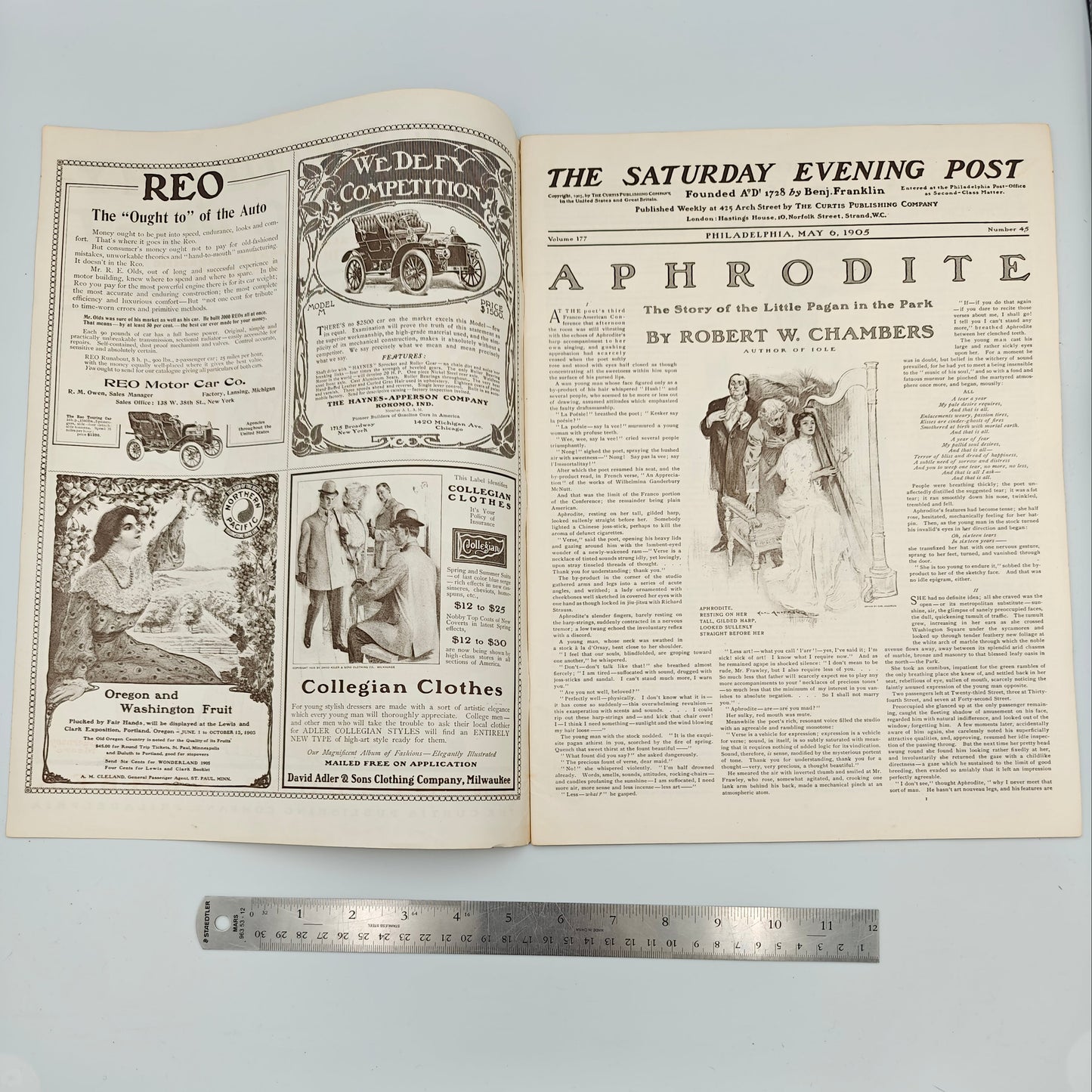 Open newspaper with visible text and images on a light blue background, with a ruler for scale. Titled "The Picknickers", this magazine features ads for REO Motor Car Co., Baynes-Apperson Co., Oregon and Washington Fruit at Lewis and Clark Exposition, Collegian Clothes by Adler and Sons.