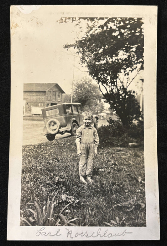 Vintage black and white photo of a child standing outdoors with a vehicle in the background