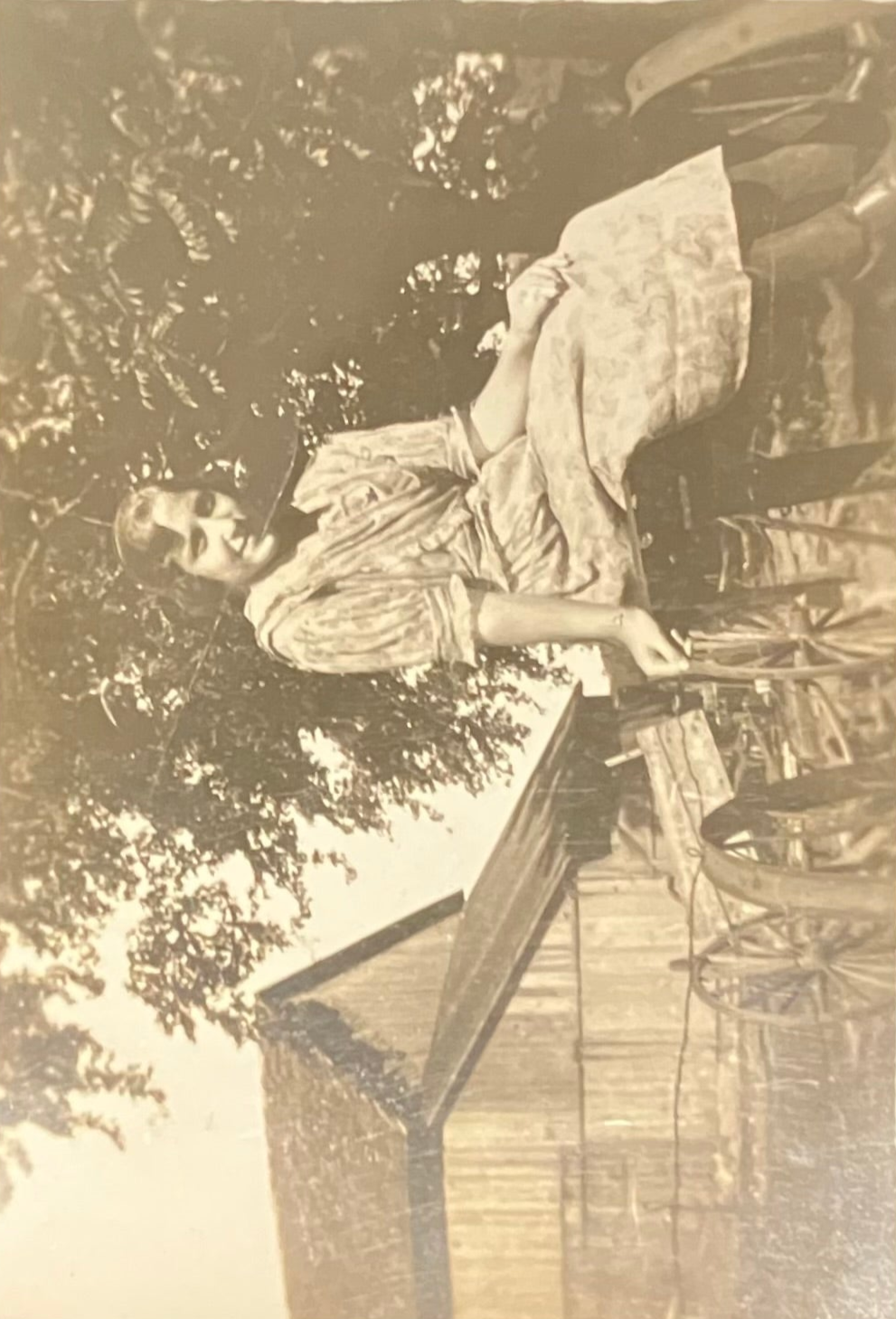 Vintage sepia-toned photograph of a person lying on grass with trees in the background