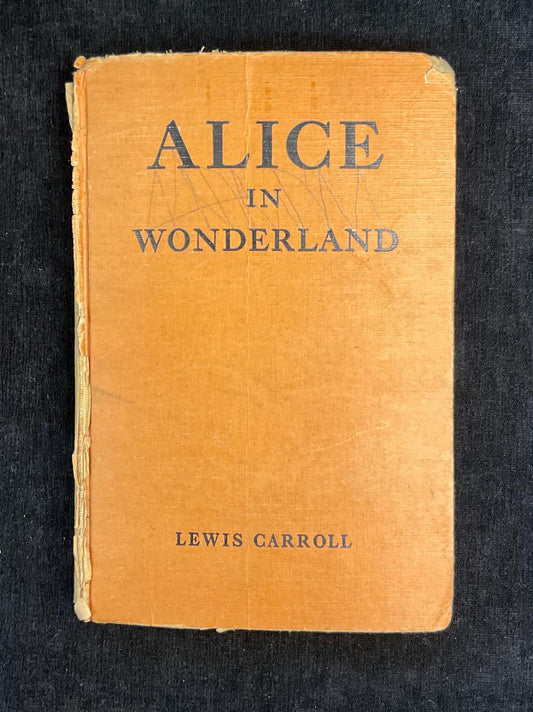 Vintage book cover of 'Alice in Wonderland' by Lewis Carroll on a dark background