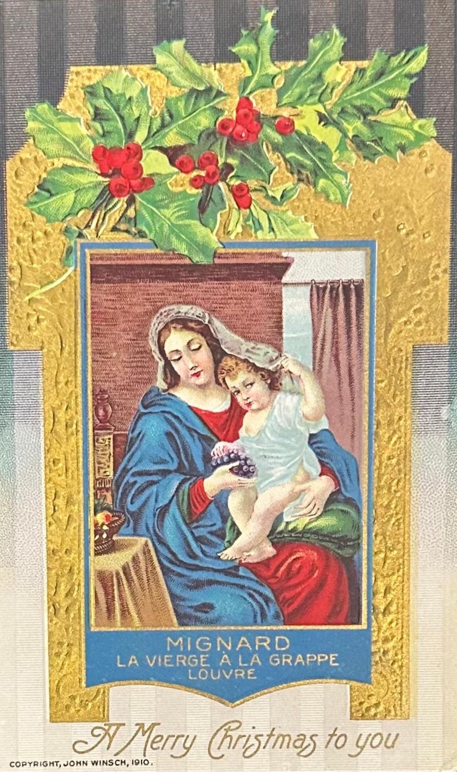 Vintage Christmas card with a religious scene of a woman holding a child, surrounded by holly leaves and berries.