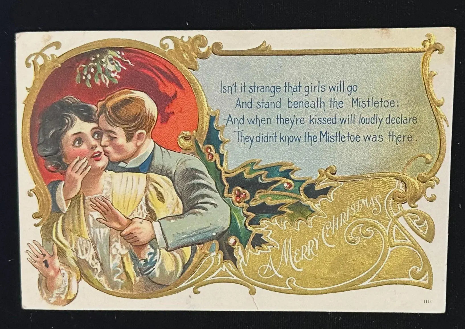 Vintage Christmas card with a couple kissing, decorative text, and mistletoe.