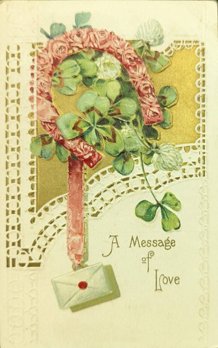 A vintage Valentine postcard featuring a horseshoe, clovers, and an envelope with a message of love. The postcard has embossed and gilded details.