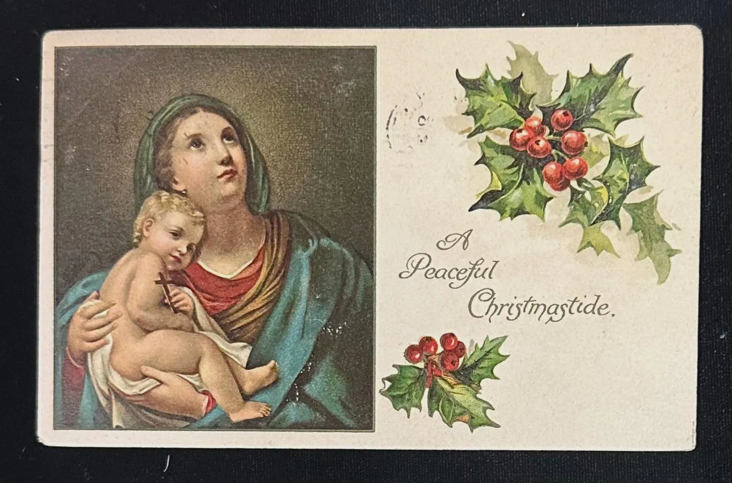 Vintage Christmas card with a depiction of a woman holding a child and holly decorations.