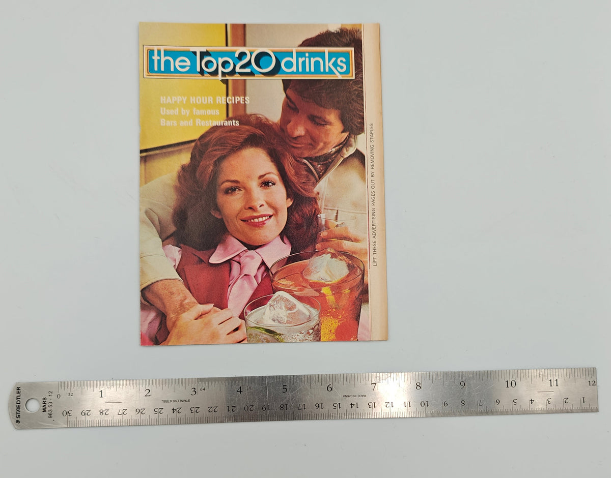 Small magazine or book with a cover featuring two people and text, next to a ruler for scale on a white background.