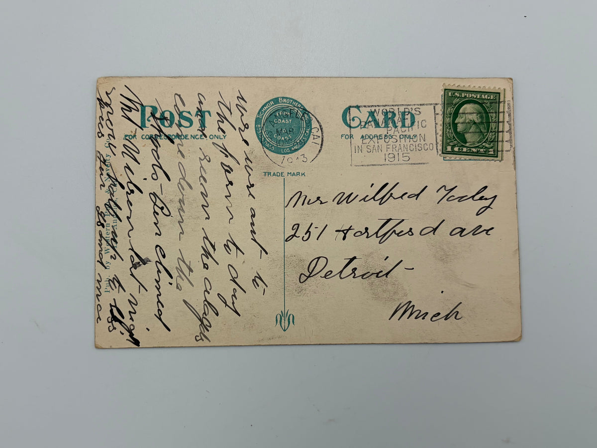 An antique vintage postcard with handwritten text, a green stamp, and a blue 'POST' label, displayed on a light gray background.