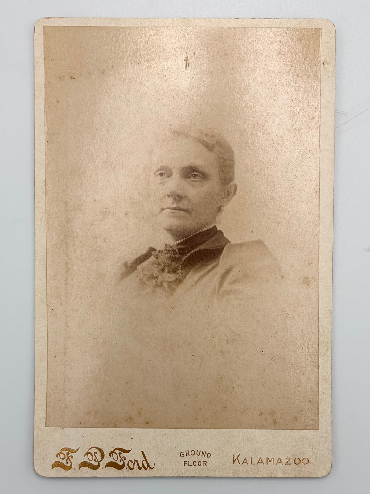 An antique cabinet card portrait of a woman, printed in sepia on aged beige paper with 'F.P. Ford Kalamazoo'