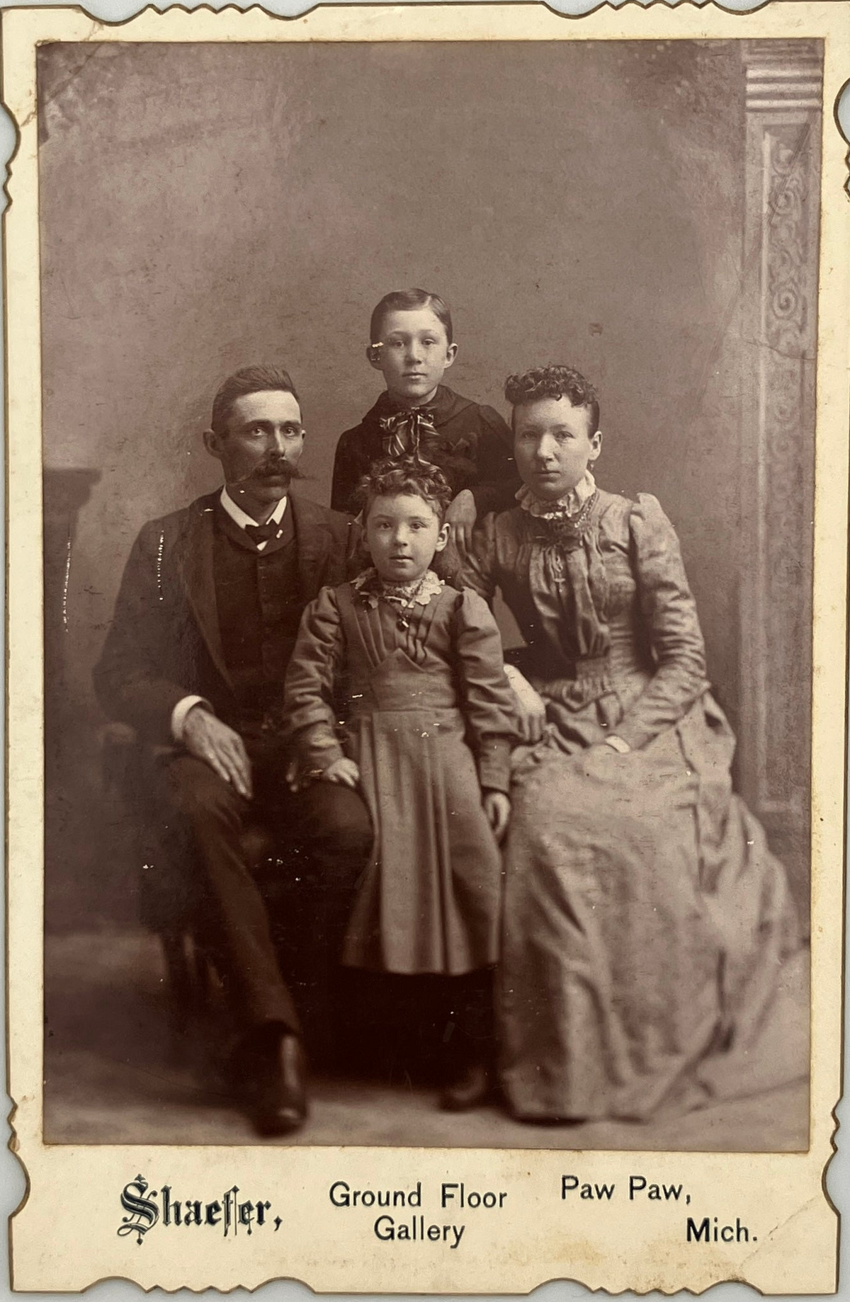 Vintage sepia family portrait print showing four people posed in a studio setting, with printed text at the bottom reading 'Shaefer, Ground Floor Paw Paw, Mich.'.