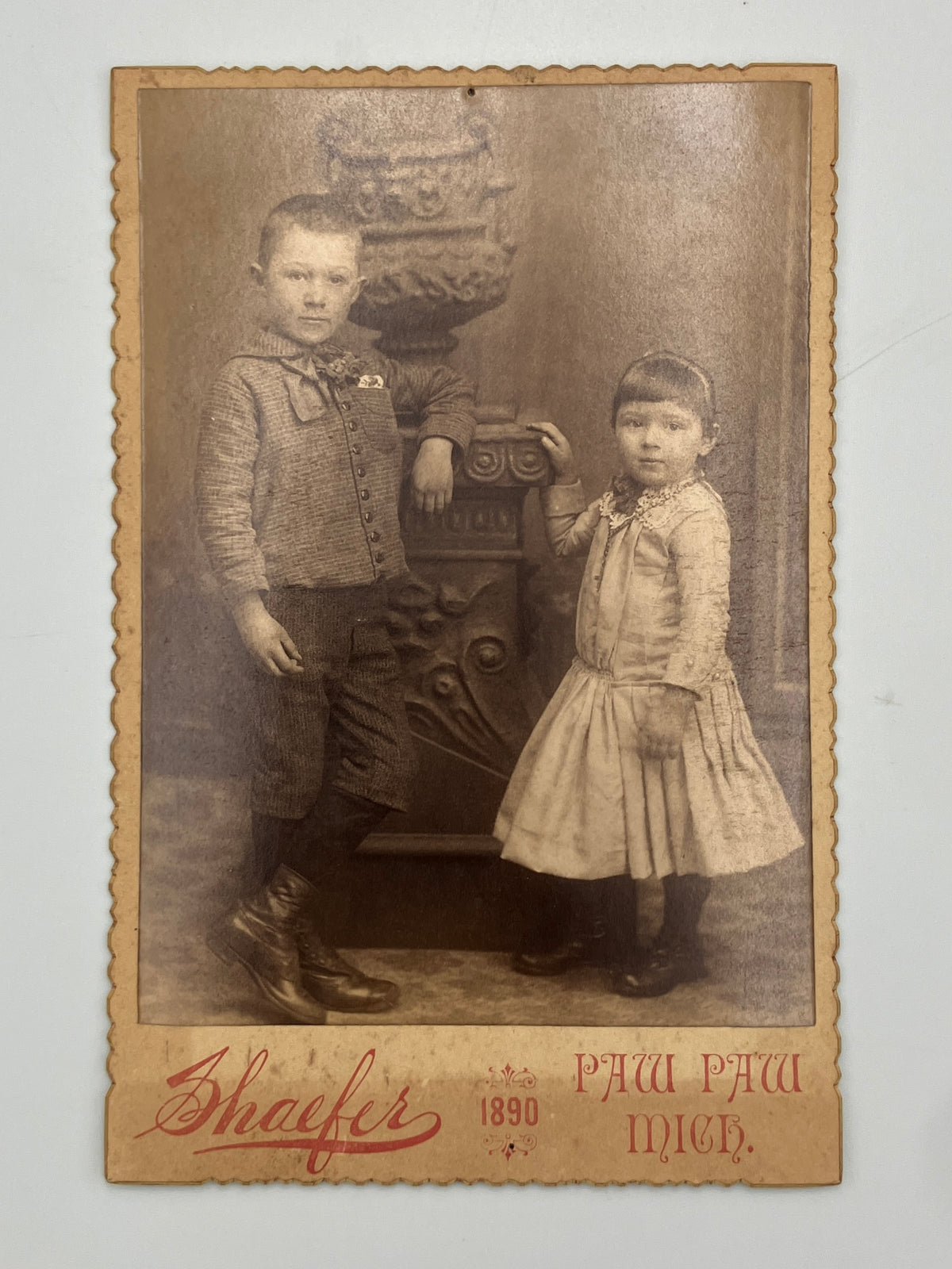 Cabinet card photo of two young siblings in 1890s children's fashion. 