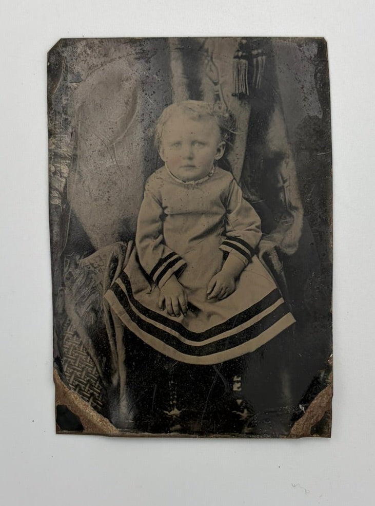 An antique black-and-white tintype portrait photograph of a seated child