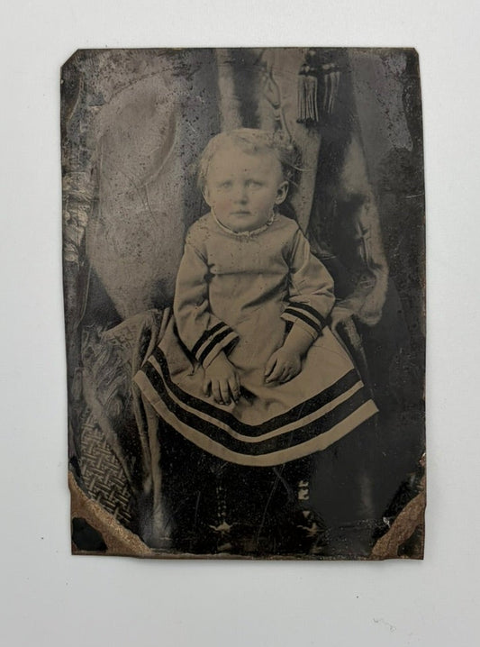 An antique black-and-white tintype portrait photograph of a seated child