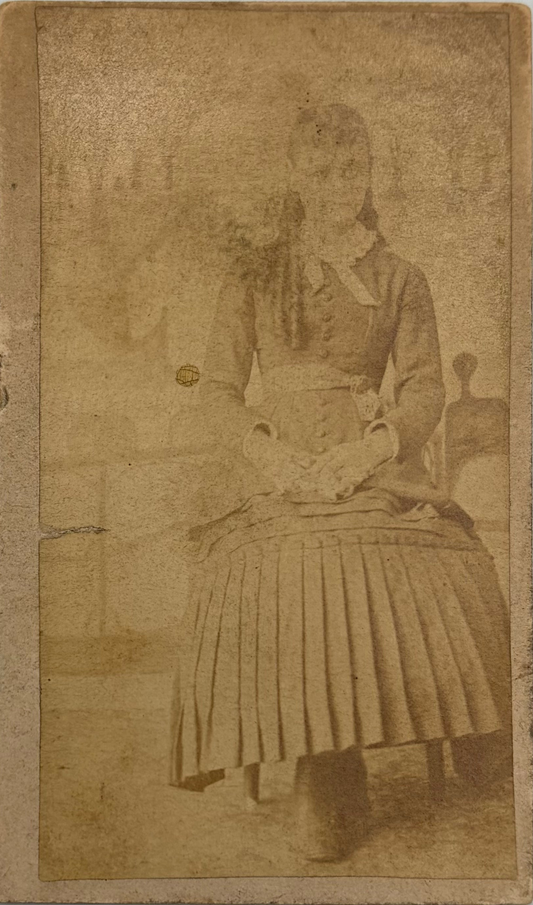An antique sepia-toned photograph showing a seated woman in a long pleated skirt and dark dress