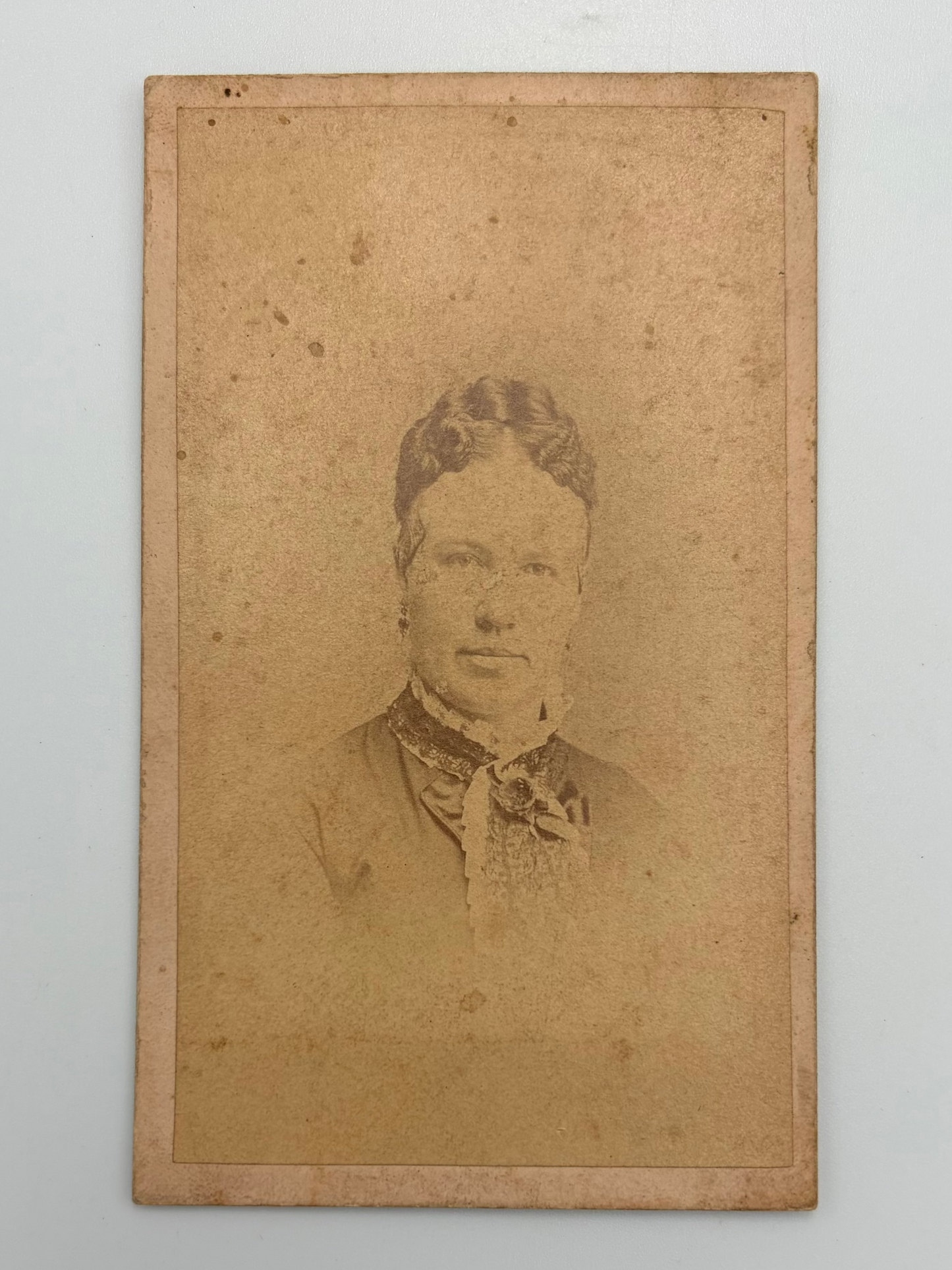 An antique carte de visite portrait featuring a sepia-toned photo of a woman, mounted on a light gray background.