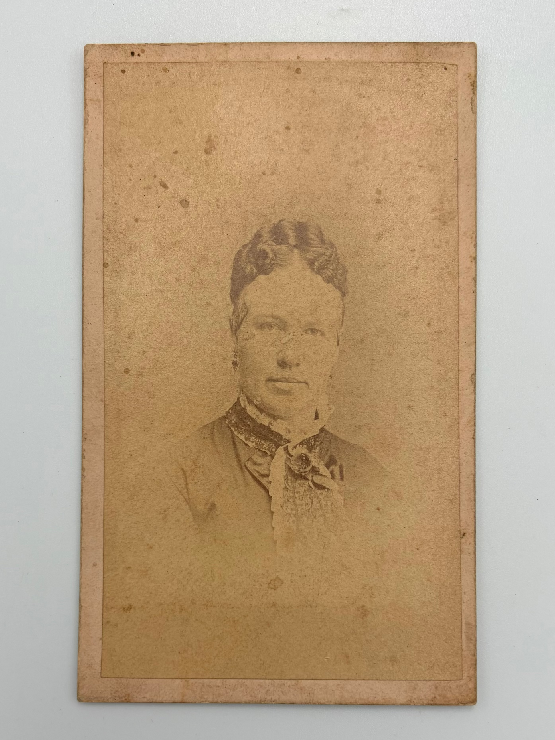 An antique carte de visite portrait featuring a sepia-toned photo of a woman, mounted on a light gray background.