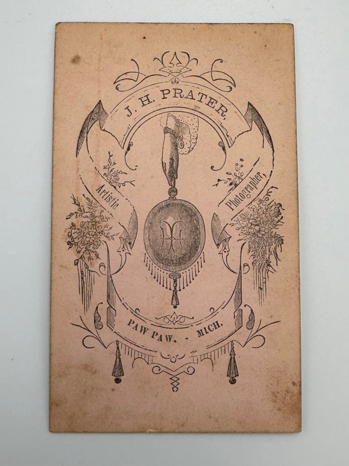 An antique brown paper card featuring a decorative black ink illustration and text, including 'J. H. Prater'