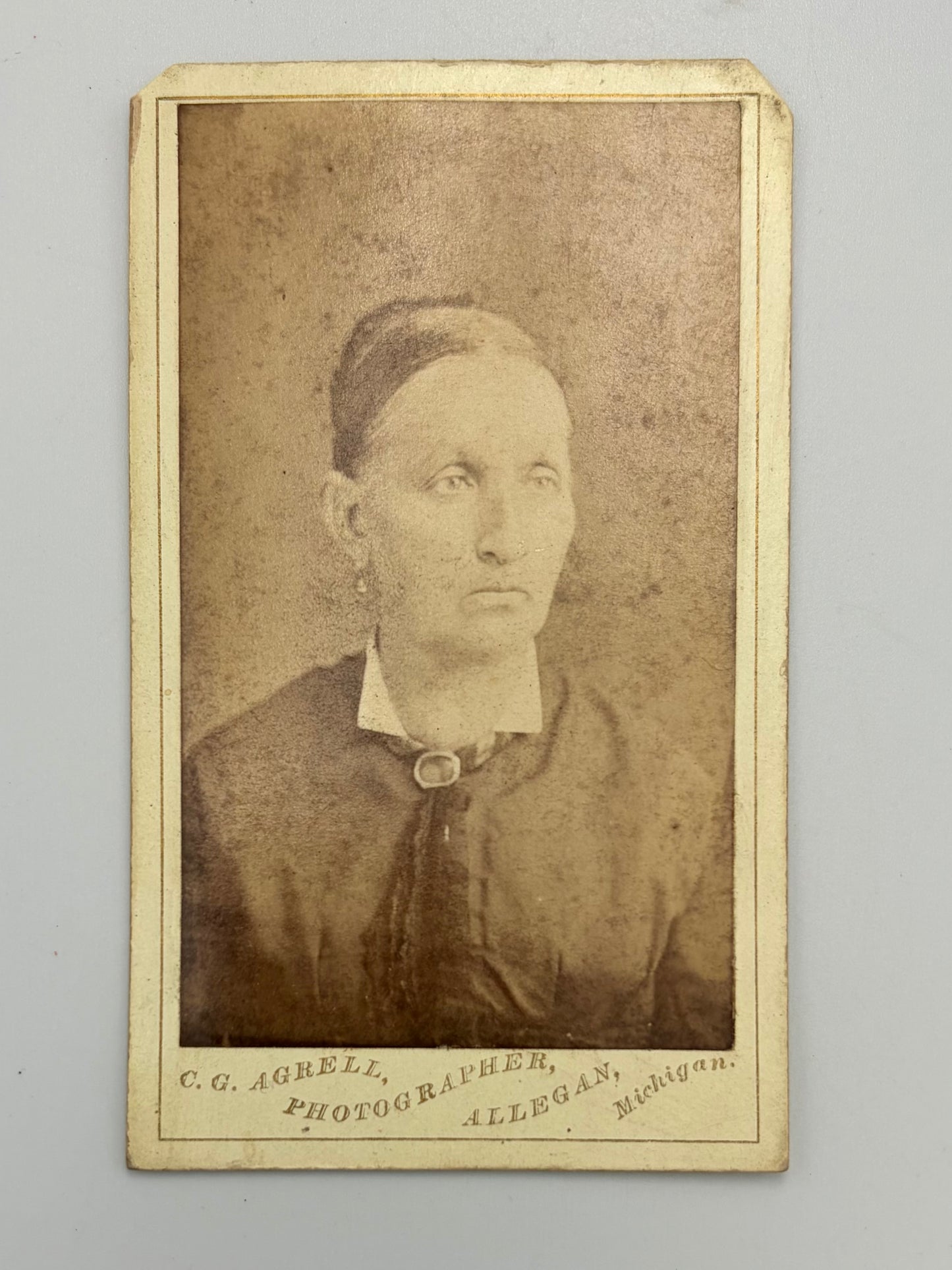 An antique sepia-toned carte de visite of a woman, mounted on a cream-colored card with photographer studio at bottom. 