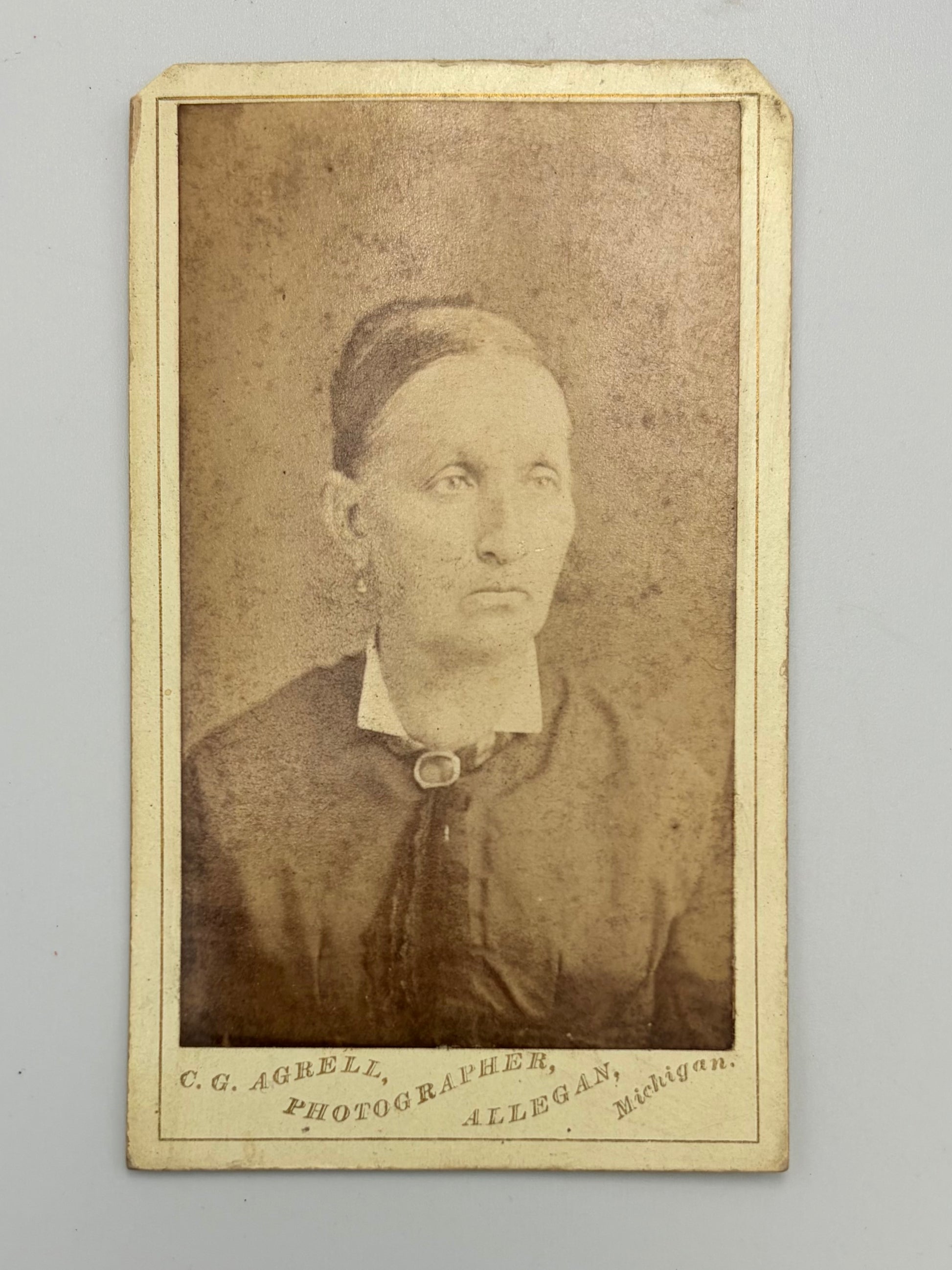 An antique sepia-toned carte de visite of a woman, mounted on a cream-colored card with photographer studio at bottom. 