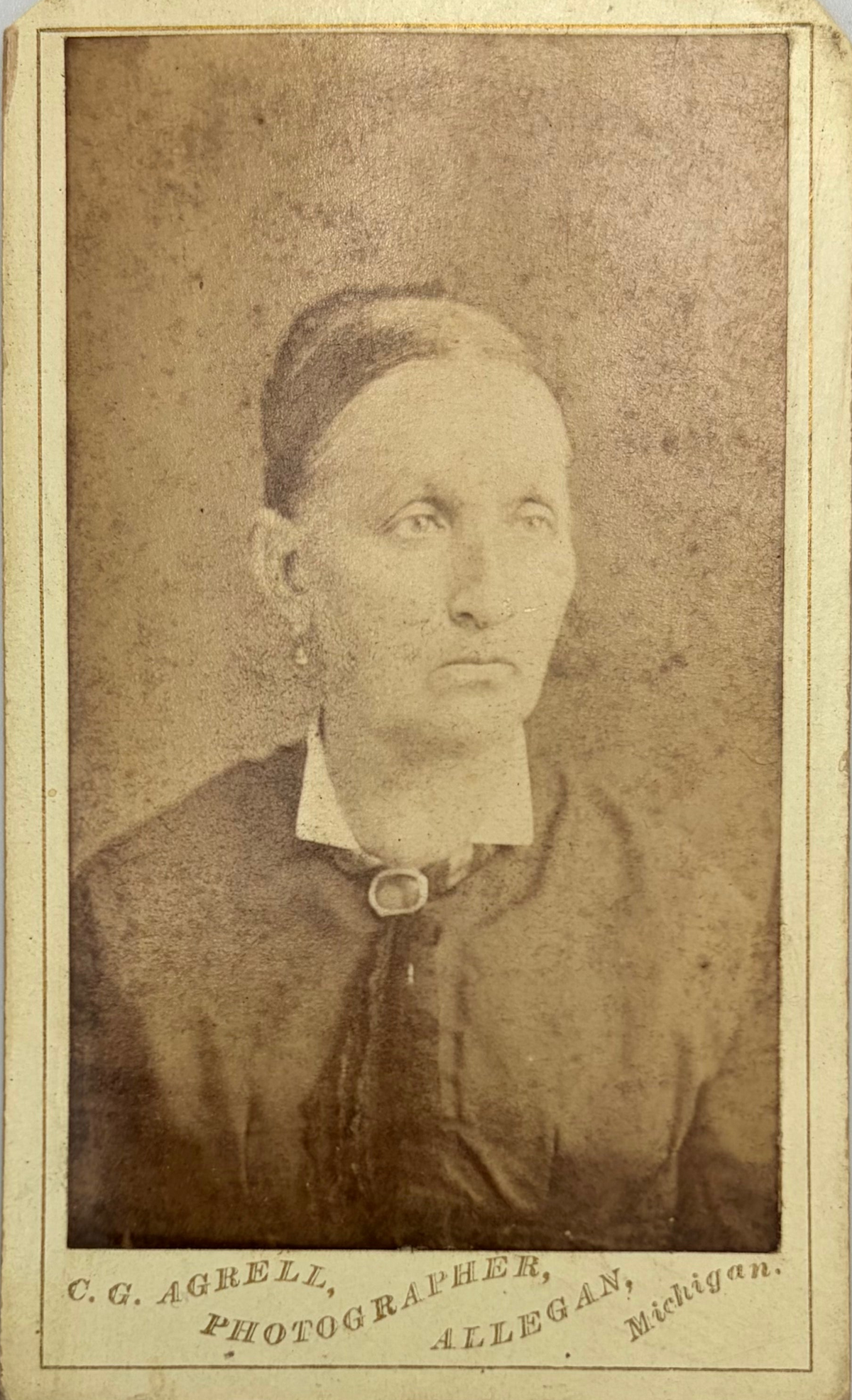 An antique sepia-toned carte de visite of a woman, mounted on a cream-colored card with photographer studio at bottom. 