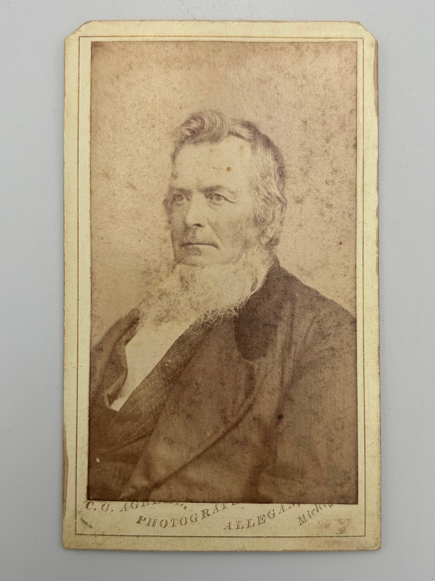 A vintage carte de visite portrait photograph print of an elderly bearded man, mounted on a cream-colored card with printed text at the bottom.