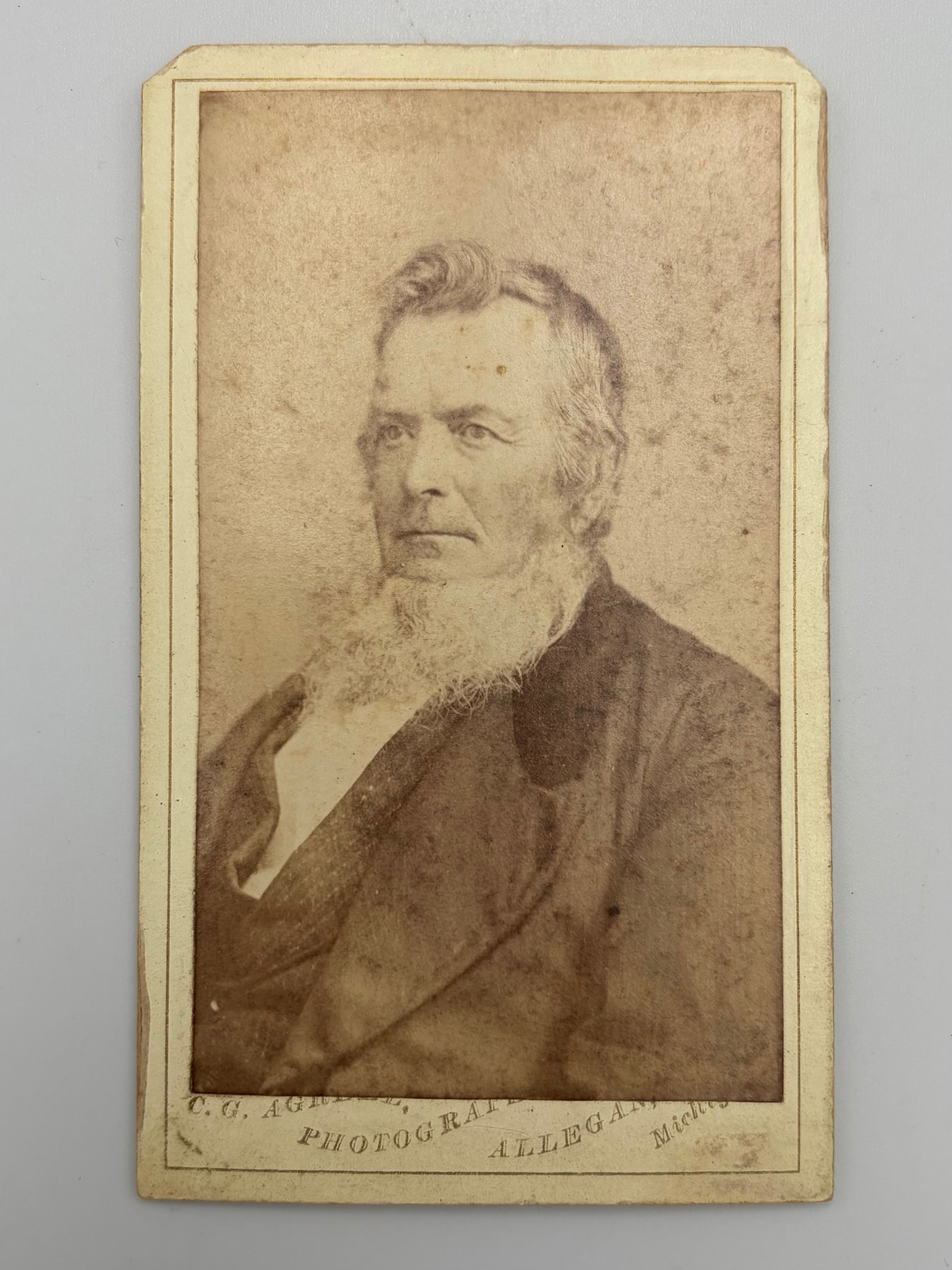 A vintage carte de visite portrait photograph print of an elderly bearded man, mounted on a cream-colored card with printed text at the bottom.