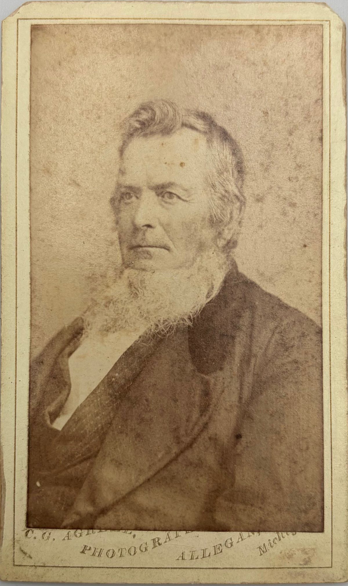 An antique sepia-toned portrait photograph print of an elderly man with a full white beard, wearing a dark coat and vest, printed on aged paper with a vintage border.