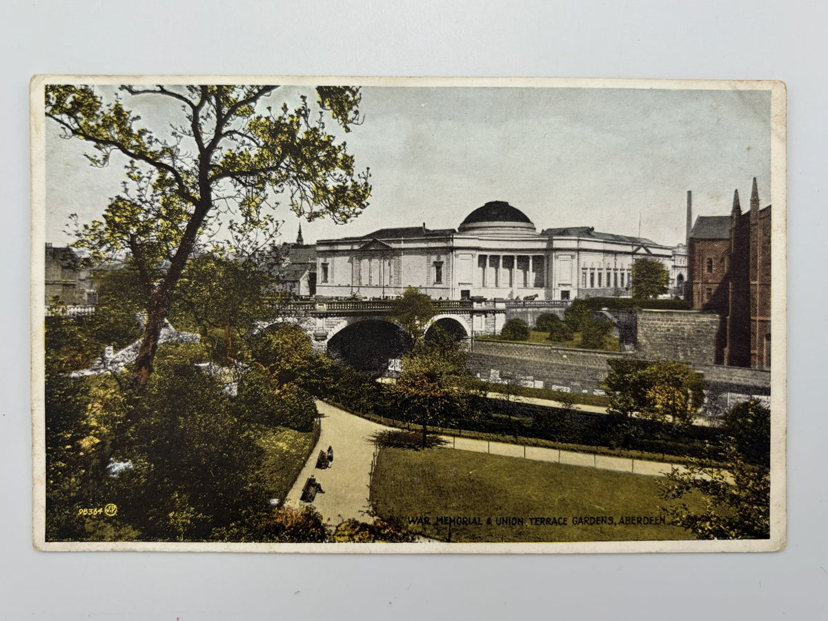 A vintage printed postcard showing an outdoor architectural scene with a large domed building across a bridge, surrounded by trees, grass, and a path in the foreground. 