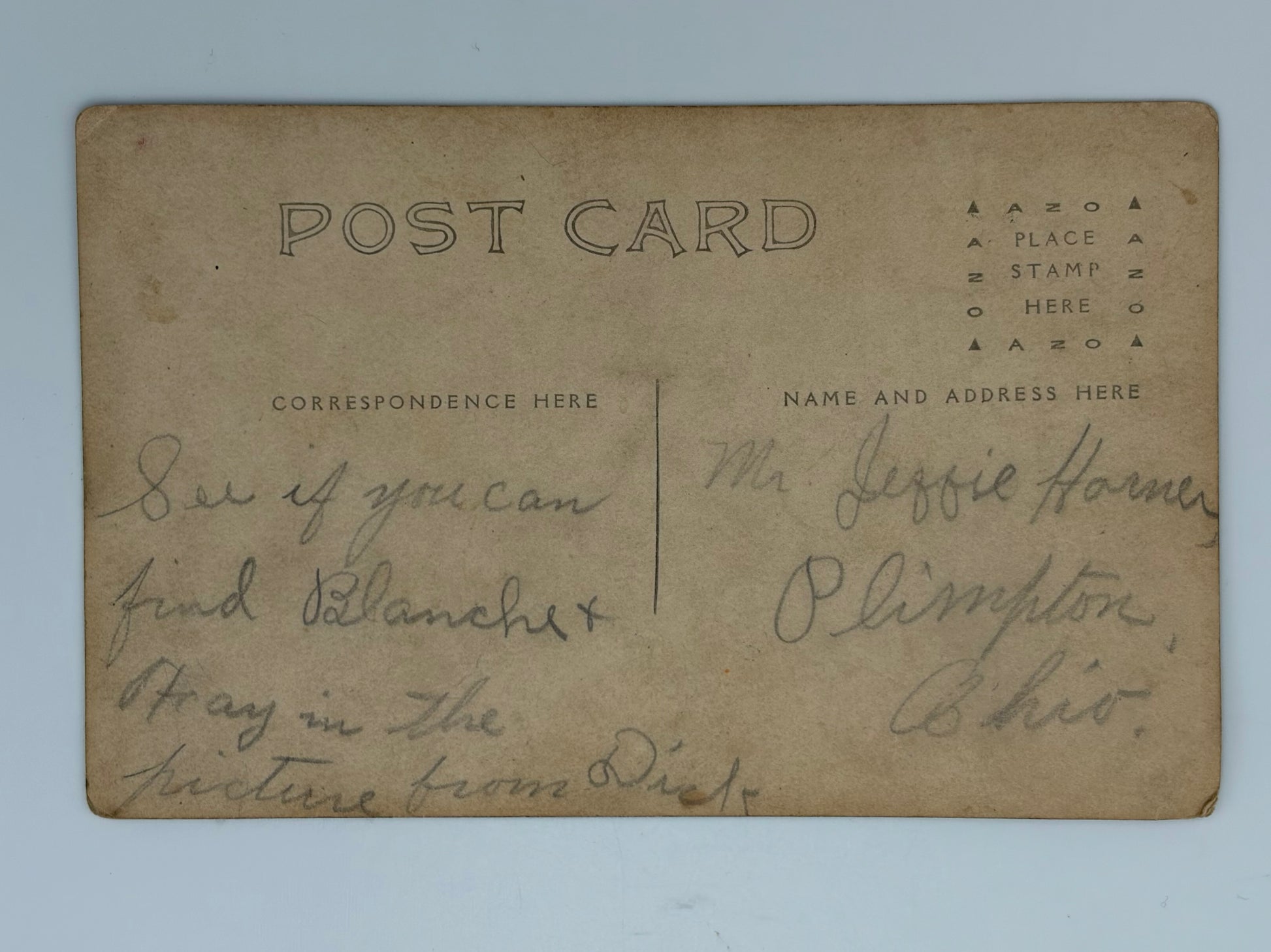 A vintage postcard with a warm tan paper background, featuring printed black text on the top and handwritten cursive writing on both sides. The postcard is photographed flat against a light blue background.