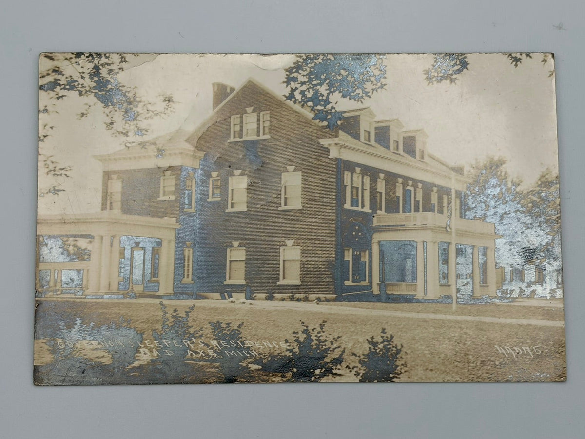 A vintage printed postcard depicting a large historic house with a porch, shown on a light gray surface